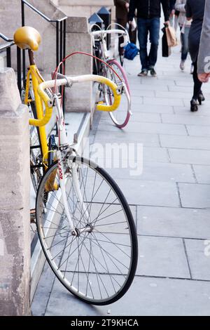 Vélo jaune appuyé contre un mur à Londres avec des piétons anonymes marchant le long du trottoir dans l'arrière-plan lointain Banque D'Images