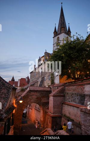 Les gens marchent au passage des escaliers pendant le crépuscule à Sibiu, Roumanie le 1 août 2023. La cathédrale luthérienne de Sibiu est également illustrée. Photo de Tim Chong Banque D'Images