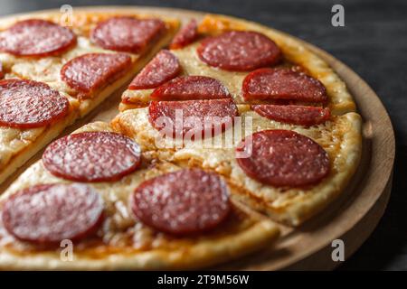 Pizza au pepperoni, coupée en morceaux, gros plan sur un support rond en bois, mise au point sélective. Banque D'Images