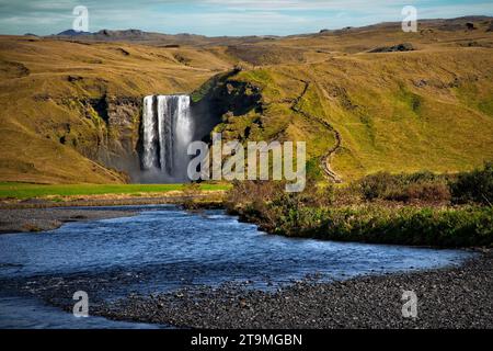 Les vistors marchent les marches jusqu'au sommet de Skogafoss, une cascade sur la rivière Skógá dans le sud de l'Islande à la falaise marquant l'ancienne côte. Banque D'Images