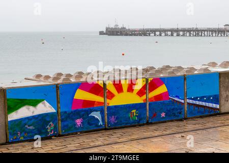 Swanage, Dorset Royaume-Uni. 26 novembre 2023. Météo Royaume-Uni : temps humide, gris et sombre à Swanage dans le Dorset. Peintures sur la barrière temporaire des vagues hivernales de Swanage les blocs de béton mis en place par l’Agence de l’environnement pour réduire l’impact des inondations, ajoutent de la couleur à une journée grise! Crédit : Carolyn Jenkins/Alamy Live News Banque D'Images