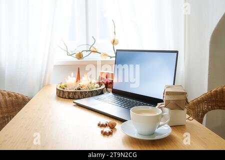 Ordinateur portable sur un bureau en bois près de la fenêtre dans un appartement grenier. Cadeaux, bougies de l'AVENT, décoration de Noël et une tasse à café. Shopping en ligne de vacances, co Banque D'Images