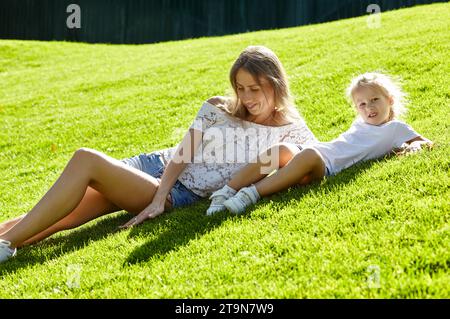 Mère avec fille allongée sur la pelouse dans le parc de la ville d'été. Enfance, loisirs et concept de personnes - repos familial heureux et passer un bon moment Banque D'Images