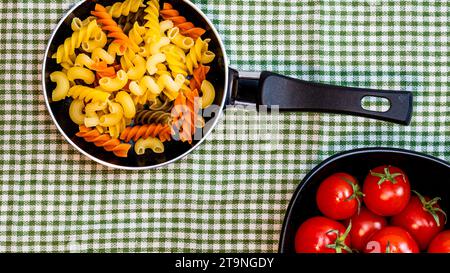 Petite petite poêle à frire avec pâtes fusilli crues tricolores dans une composition rustique. Banque D'Images