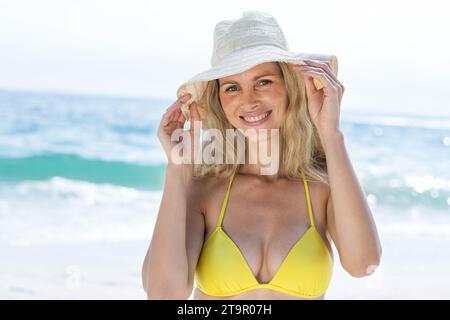 Souriant jolie blonde en bikini regardant la caméra à la plage Banque D'Images