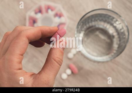 Femme trier les pilules Organiseur des injections hebdomadaires gros plan de la boîte de pilules médicales avec des doses de comprimés pour la journée prendre des médicaments avec des médicaments blancs roses et des capsules. Jeune femme qui reçoit ses vitamines quotidiennes à la maison. Médicaments compléments alimentaires, immunité et prévention des maladies huile de poisson gel Softgel, vitamine D et C minéraux oméga, fibres, acides aminés gras, probiotiques sédatifs. Les soins de santé et les maladies guérissent Banque D'Images
