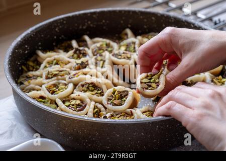 Mains tenant Qatayef rempli de chocolat et garni de pistaches sur une table en bois, avec une assiette à préparer au four plus tard comme Ramadan swe Banque D'Images