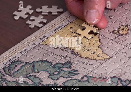 Un gros plan des mains d'une dame retraitée résolvant un puzzle d'une carte du Groenland Banque D'Images
