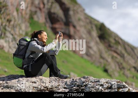 Randonneur prenant des photos avec smartphone assis dans la nature Banque D'Images