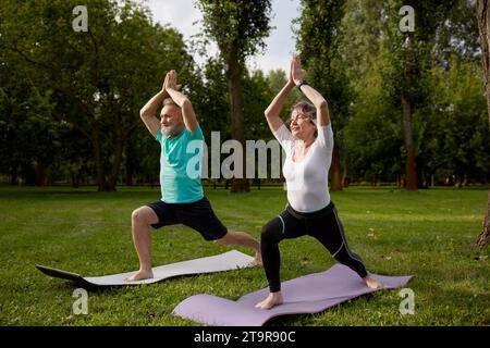 Couple plus âgé actif faisant des exercices de yoga à l'extérieur au parc de la ville Banque D'Images