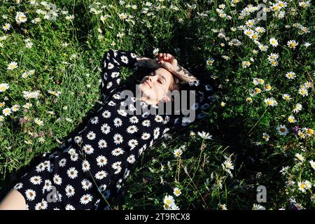 une femme dans une robe dans une fleur se trouve sur un champ avec des marguerites Banque D'Images