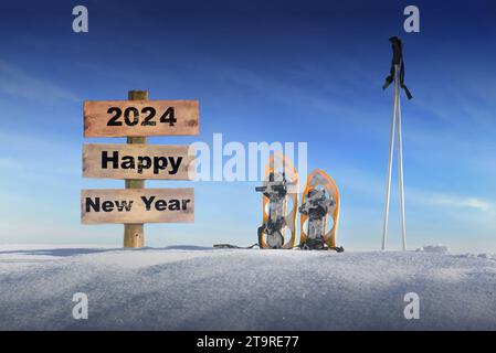 panneau en bois avec texte bonne année 2024 dans la neige à côté de raquettes et bâtons de ski sous le ciel bleu Banque D'Images