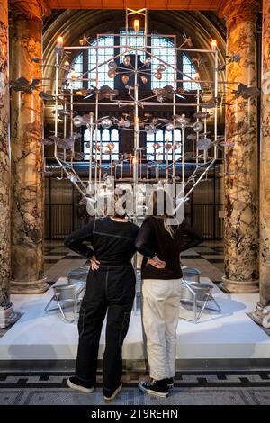 Londres, Royaume-Uni. 27 novembre 2023. L’installation 2023 Christmas Tree, réalisée par les designers londoniennes Isabel Gibson et Helen Chesner (Isabel + Helen), est dévoilée au V&A. Inspirée par le ciel nocturne scintillant, l'installation présente un système complexe de turbines alimentées par le vent, chacune tournant dans sa propre orbite pour alimenter collectivement douze lumières qui se trouvent dans la structure. Un jeu délicat d'hélices en formation équilibrée imite les systèmes célestes qui pendent dans le ciel, transférant l'énergie du vent en lumière. Crédit : Stephen Chung / Alamy Live News Banque D'Images