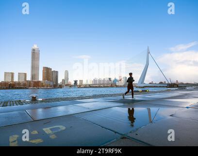 femme jogging sur le remblai de la rivière nieuwe maas près du pont erasmus vu du front de mer de kop van zuid dans la ville néerlandaise de rotterdam sur une journée ensoleillée avec Banque D'Images