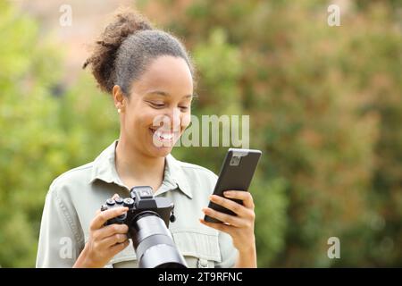 Heureux photographe noir vérifiant le contenu du téléphone dans un parc Banque D'Images