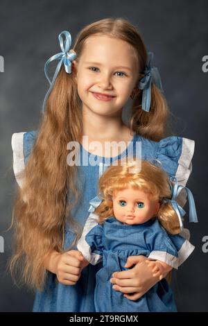 Portrait de ?ute fille enfant et poupée isolé sur fond gris. Enfant et jouet préféré. Un cadeau pour un anniversaire ou d'autres vacances. Banque D'Images