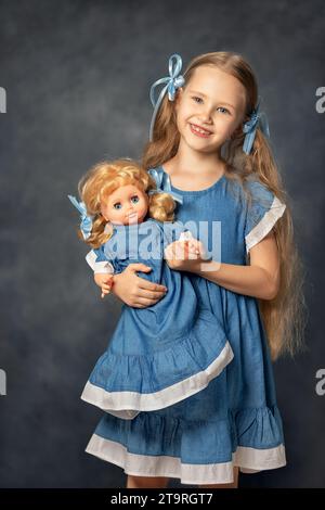 Portrait de ?ute fille enfant et poupée isolé sur fond gris. Enfant et jouet préféré. Un cadeau pour un anniversaire ou d'autres vacances. Banque D'Images