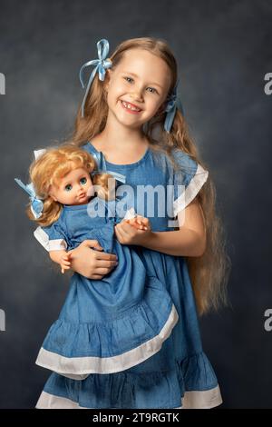 Portrait de ?ute fille enfant et poupée isolé sur fond gris. Enfant et jouet préféré. Un cadeau pour un anniversaire ou d'autres vacances. Banque D'Images