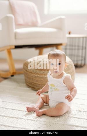 Heureuse petite fille assise sur le plancher de la pépinière neutre à la maison Banque D'Images