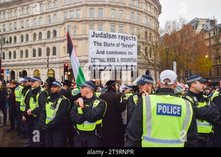 Londres, Royaume-Uni. 26 novembre 2023. Des policiers entourent des Juifs ultra-orthodoxes anti-sionistes et pro-palestiniens tenant une pancarte qui déclare "le judaïsme rejette l'État d'Israël" qui organisent une contre-manifestation à Trafalgar Square. Des milliers de manifestants pro-israéliens ont défilé dans le centre de Londres contre l’antisémitisme et ont appelé à la libération des otages israéliens détenus par le Hamas à Gaza. (Photo de Vuk Valcic/SOPA Images/Sipa USA) crédit : SIPA USA/Alamy Live News Banque D'Images