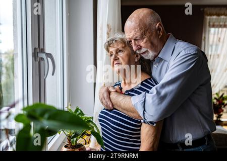 Portrait de couple senior regardant par la fenêtre à la maison Banque D'Images