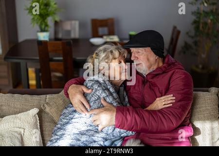 Couple âgé portant des vêtements d'hiver à l'intérieur de la maison en raison des prix élevés de l'électricité Banque D'Images