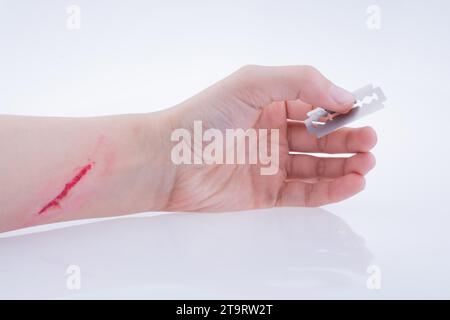 Main blessée tenant une lame de rasoir sur fond blanc Banque D'Images