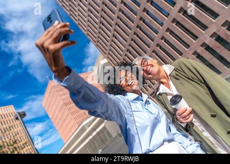 Photo dynamique à faible angle de vue de femmes d'affaires multiculturelles prenant un selfie souriant à la caméra à l'extérieur Banque D'Images