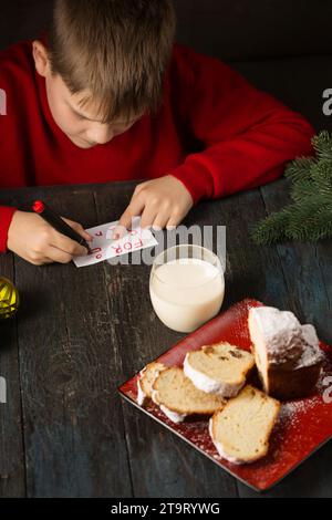 Un petit garçon écrit une note au Père Noël et prépare un régal Banque D'Images