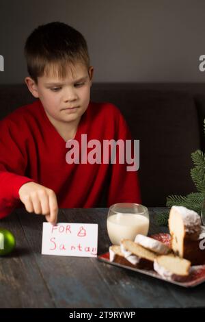 Un petit garçon écrit une note au Père Noël et prépare un régal Banque D'Images