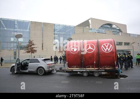 Berlin, Allemagne. 27 novembre 2023. Des militants de l’organisation environnementale Greenpeace conduisent un grand tonneau portant les logos des constructeurs automobiles BMW (de gauche à droite), Mercedes-Benz et Volkswagen devant la Chancellerie fédérale avant le sommet automobile. La chancelière Scholz rencontre des représentants de l’industrie automobile pour discuter de la poursuite de l’expansion de la mobilité électrique sur les routes allemandes. Crédit : Hannes P Albert/dpa/Alamy Live News Banque D'Images