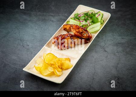 Plat européen. Poulet en sauce, avec pommes de terre frites et salade de concombre, herbes et oignons. vue latérale arrière-plan sombre Banque D'Images