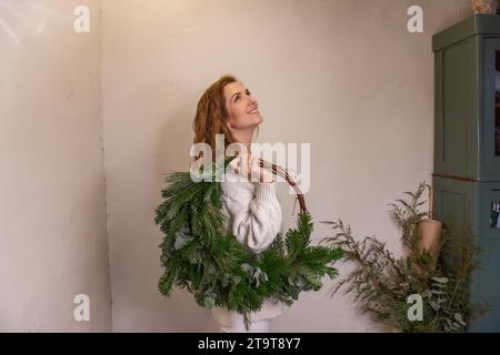 Portrait de jeune femme tenant une couronne de Noël verte asymétrique faite de matériaux naturels sur l'épaule dans les mains. Fille en beige tricoté avec Homemad Banque D'Images