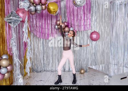 Dansant fille de mode folle avec maquillage de beauté, dans un pantalon rose doux, body en maille parmi les confettis, scintillant en aluminium brillant argenté. Les modèles s'amusent avec Glit Banque D'Images