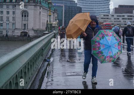 Londres Royaume-Uni. 27 novembre 2023. Un homme lutte avec deux parapluies sur le pont de Westminster pendant les fortes pluies dans la capitale .crédit : amer ghazzal/Alamy Live News . Banque D'Images