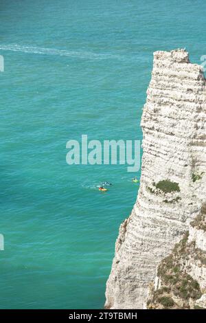 Une falaise blanche imposante se démarque de la mer bleu saphir avec des gens jouant au bateau banane à Étretat Banque D'Images