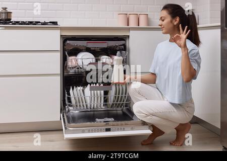 femme verse le liquide de rinçage dans le compartiment lave-vaisselle dans la cuisine blanche moderne Banque D'Images