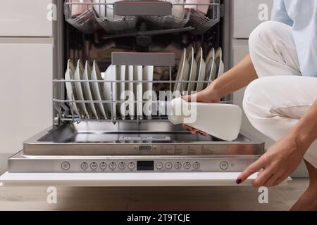 la main féminine verse le liquide de rinçage dans le compartiment lave-vaisselle de la cuisine blanche moderne Banque D'Images