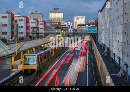 Essen, Nordrhein-Westfalen, Deutschland - Autobahn A40 in der Innenstadt, Ausfahrt Essen Zentrum, waehrend der Abenddaemmerung. U-Bahn Linie U18 auf dem Weg zum Berliner Platz haelt an U-Bahn Station Savignystrasse. Rechts Wohnhaeuser hinter Schallschutzwand. An der Hauswand befindet sich eine LANUV Luftmessstation, Essen Kruppstraße 117 EKRU2, rechts unter der Laterne. Anwohner werden durch Laerm und Abgase belastet. Hinten Gebaeude mit Schriftzug Postbank, Eon und Evonik. Essen Nordrhein-Westfalen Deutschland *** Essen, Rhénanie du Nord-Westphalie, Allemagne Autobahn A40 dans le centre-ville, sortie es Banque D'Images