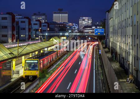 Essen, Nordrhein-Westfalen, Deutschland - Autobahn A40 in der Innenstadt, Ausfahrt Essen Zentrum, waehrend der Abenddaemmerung. U-Bahn Linie U18 auf dem Weg zum Berliner Platz haelt an U-Bahn Station Savignystrasse. Rechts Wohnhaeuser hinter Schallschutzwand. An der Hauswand befindet sich eine LANUV Luftmessstation, Essen Kruppstraße 117 EKRU2, rechts unter der Laterne. Anwohner werden durch Laerm und Abgase belastet. Hinten Gebaeude mit Schriftzug Postbank, Eon und Evonik. Essen Nordrhein-Westfalen Deutschland *** Essen, Rhénanie du Nord-Westphalie, Allemagne Autobahn A40 dans le centre-ville, sortie es Banque D'Images