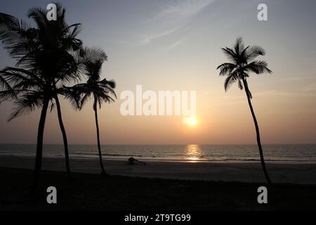 Une silhouette de cocotiers et un bateau de pêche sur la plage alors que le soleil se couche à Colva Beach à Goa, en Inde Banque D'Images