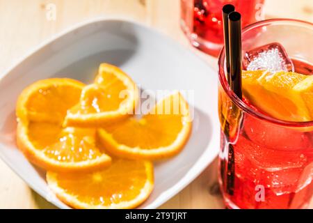 gros plan d'un verre de spritz apéritif cocktail aperol avec tranches d'orange et glaçons sur table en bois près d'une assiette de tranches d'oranges Banque D'Images