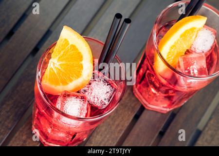 gros plan de la vue de verres de spritz apéritif cocktail rouge aperol avec tranches d'orange et glaçons sur table en bois Banque D'Images