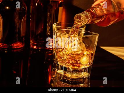 barman versant le whisky devant le verre à whisky et les bouteilles sur la table noire Banque D'Images