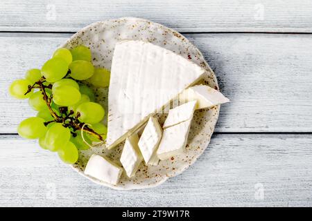 Assiette d'argile faite à la main de fromage camembert et raisins sur un fond en bois bleu. Vue de dessus, Banque D'Images