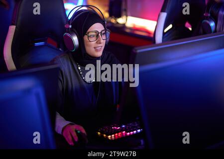 Portrait en grand angle de jeune femme musulmane jouant à des jeux vidéo dans le club de cybersports et portant des écouteurs pro, espace de copie Banque D'Images