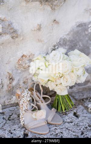 Bouquet de mariage se tient près d'un mur de pierre antique à côté des chaussures de la mariée Banque D'Images