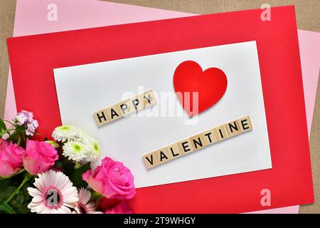 Carte de voeux de Saint-Valentin. Coeur rouge, bouquet de fleurs roses et lettres Happy Valentine sur fond de papier blanc, composition de pose plate. Banque D'Images