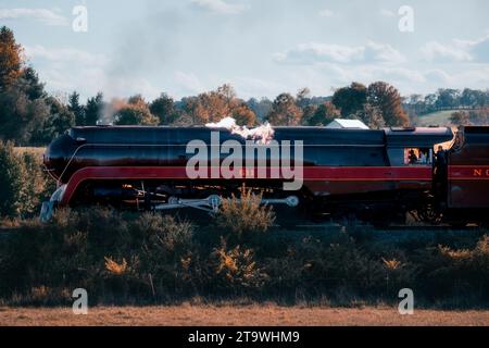 Une locomotive à vapeur noire et rouge de style vintage et des voitures de tourisme garées sur une voie ferrée dans un environnement rural pittoresque, prêtes pour un voyage Banque D'Images