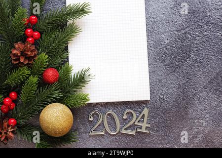 Bonne année 2024, fond gris avec branche de sapin et bloc-notes carte de vacances du nouvel an, bannière, vue de dessus, espace vide. Espace de copie. Branche de Noël an Banque D'Images